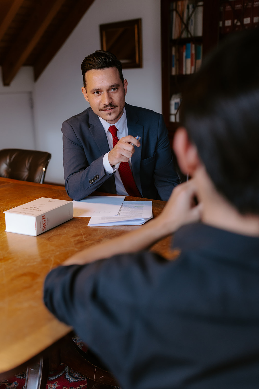 Maximilian Schüßler und ein Mandant unterhalten sich während eines Termins an einem Tisch in der Kanzlei